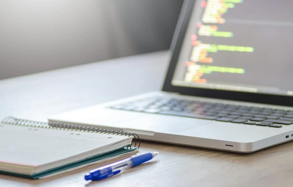 Close-up of a laptop with code, notebook, and pen